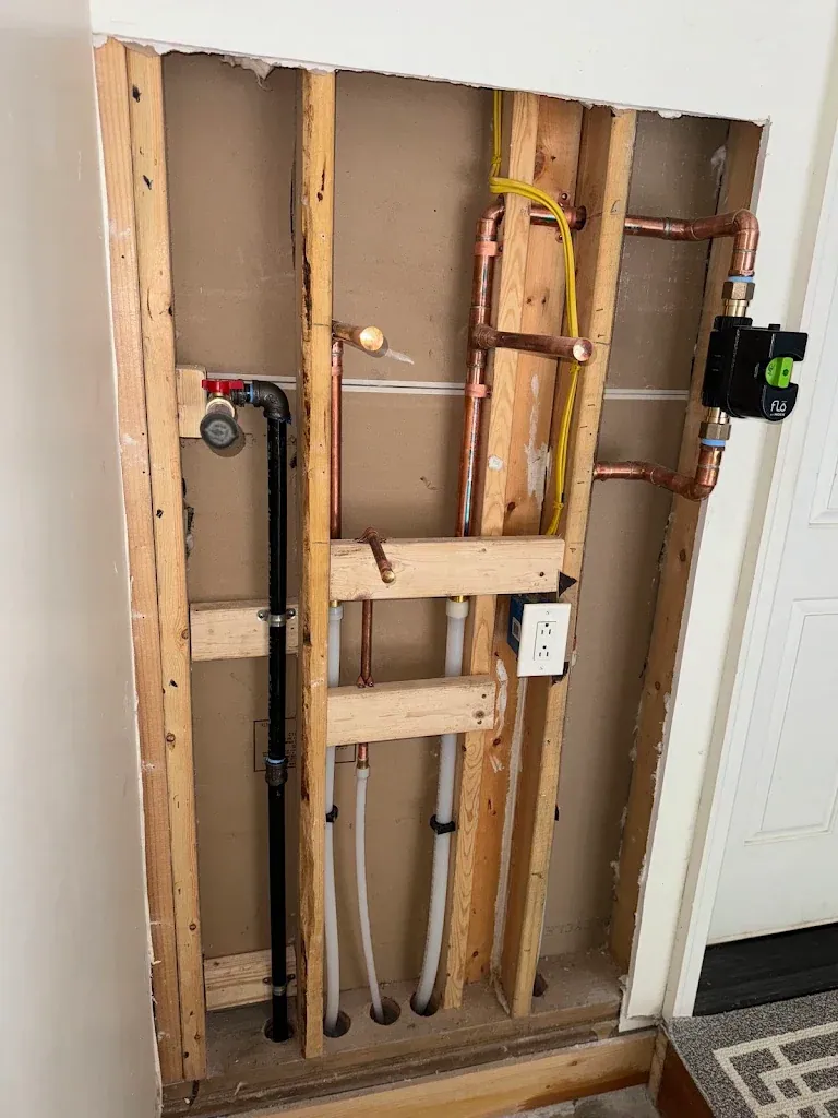 Open wall showing copper and PEX supply lines, a black ABS drain and a Flo by Moen smart water shutoff