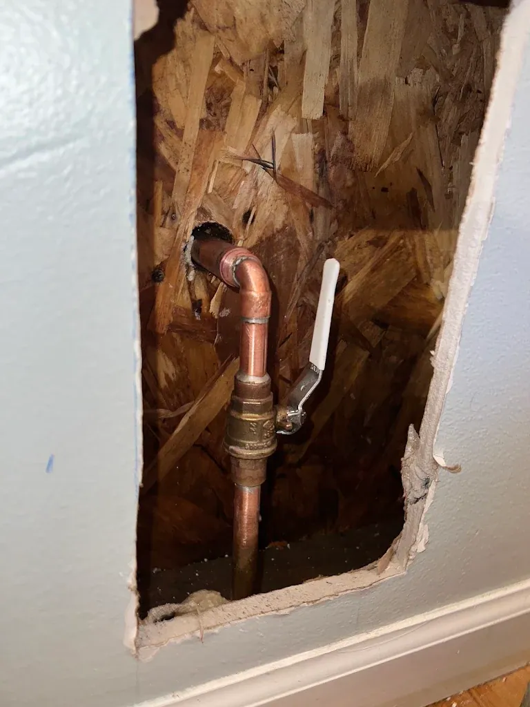 Copper pipe and new shutoff valve exposed in a cut-open section of drywall