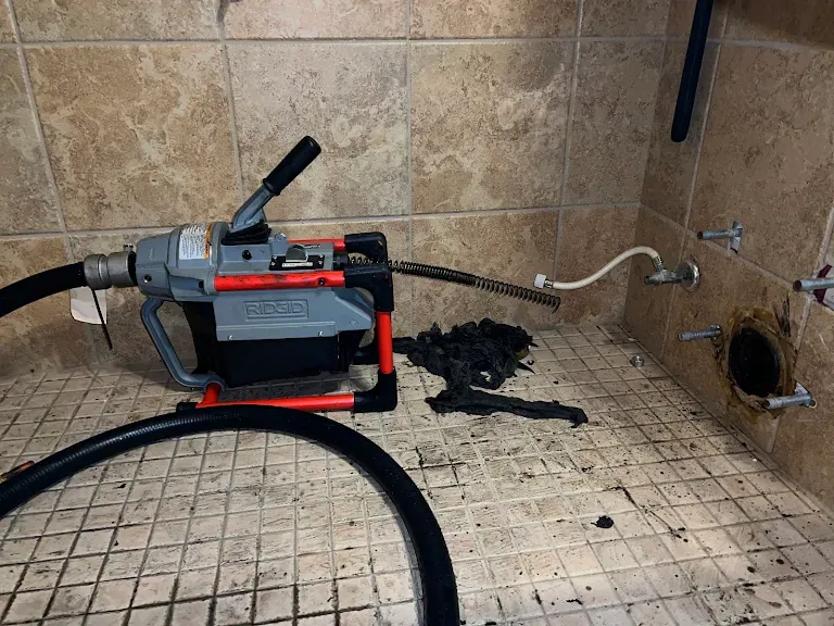 RIDGID sectional drain machine clearing a toilet drain with the toilet pulled and debris on the tile floor