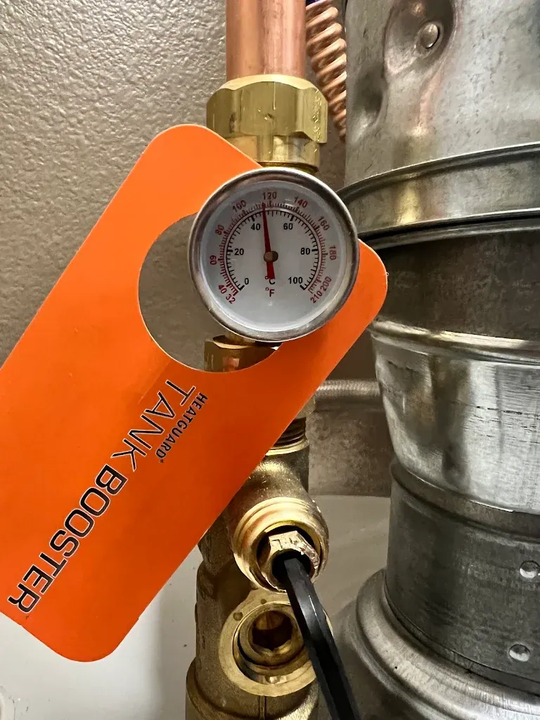 Thermometer reading on a water heater outlet next to a tank booster thermostatic mixing valve tag