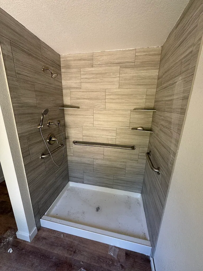 Tiled walk-in shower with handheld shower, shelves and grab bars seen from the doorway