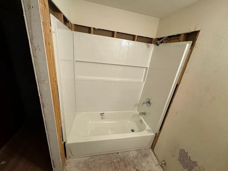 New bathtub and subway-tile-look surround installed in a bathroom under renovation