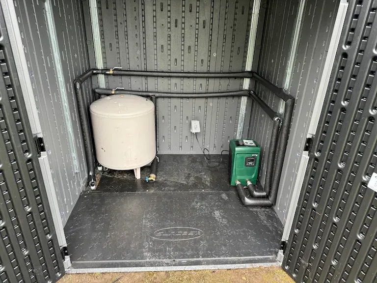 Well pressure tank and green DAB booster pump installed in a resin storage shed with insulated piping